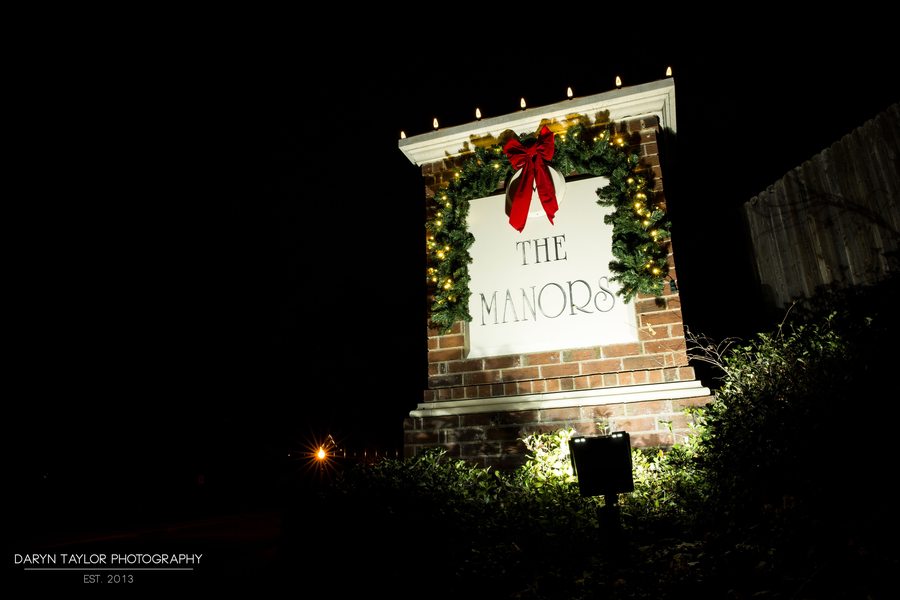 Neighborhood subdivision entrance monument decorated with holiday garland, red bow and warm white candle lights at night
