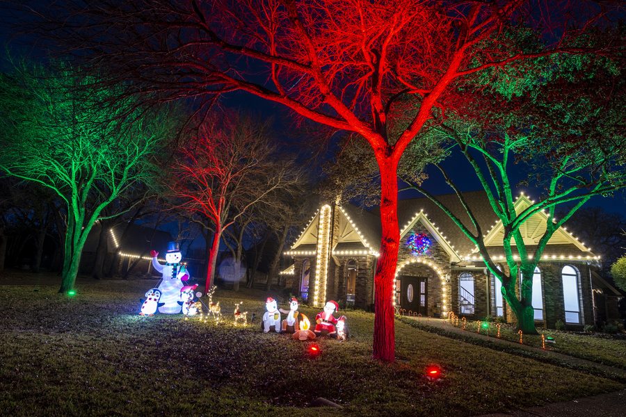 Trees uplighted in red and green RGB holiday colors with Christmas inflatables and roofline lights