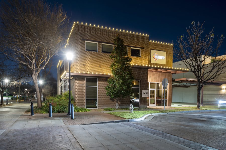 Downtown brick commercial building with warm white holiday lights along roofline and canopy at night