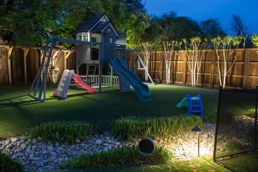 Play set and turf lit with discreet path lighting along the fence line