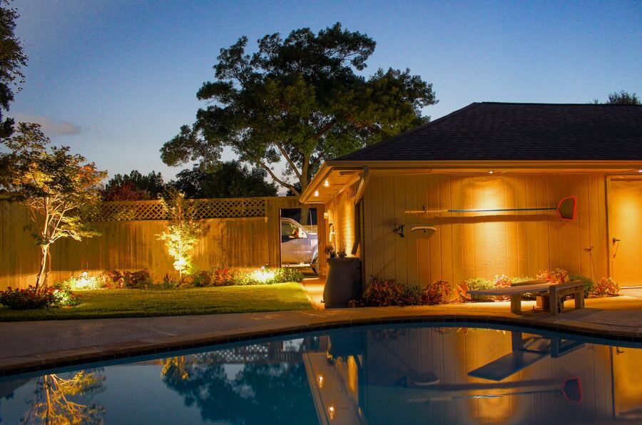 Pool house and tree uplighting reflected in the pool at dusk