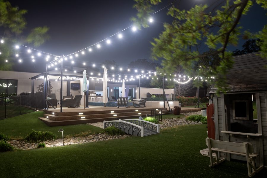 String lights over a multi-level deck with bridge and garden at night