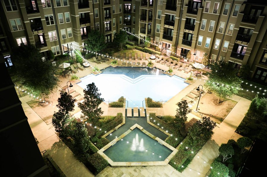 Aerial night view of luxury apartment pool courtyard lit with string lights across the full amenity deck